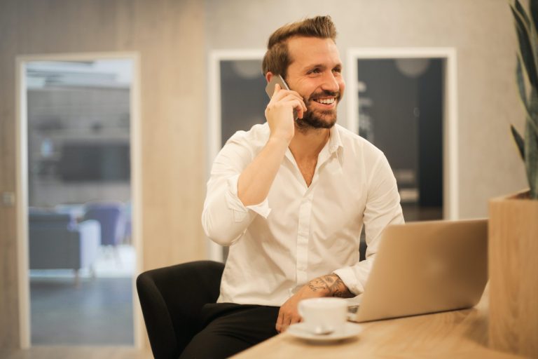 Hombre sonriente hablando por teléfono junto a un portátil – Alta de trabajadores