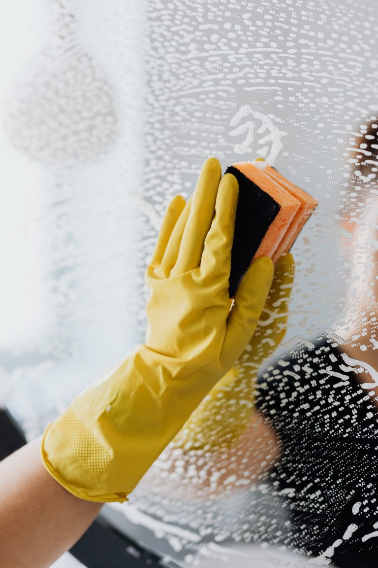 Mano con guante amarillo limpiando un cristal – Empleado de hogar