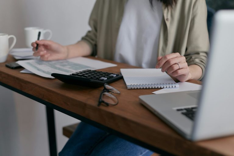 Persona anotando gastos junto a una calculadora y un portátil – Guía de gastos deducibles de un autónomo