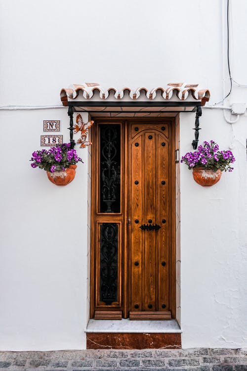 Puerta de madera con macetas de flores en una fachada blanca – Donaciones