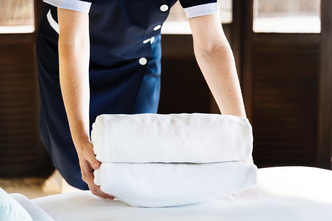 Persona colocando toallas blancas en una cama – Empleado de hogar