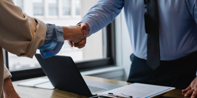 Apretón de manos sobre una mesa con contrato y portátil – Actualidad laboral: Reforma laboral 2022: contratos y reglas vigentes
