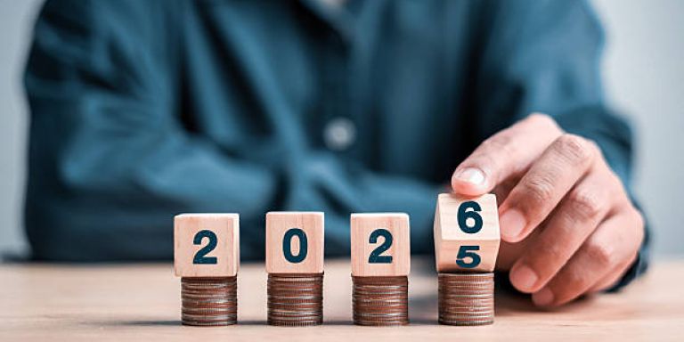 Mano colocando bloques de madera sobre monedas para formar el año 2026 – Actualidad laboral: Calendarios Laborales 2026 Burgos